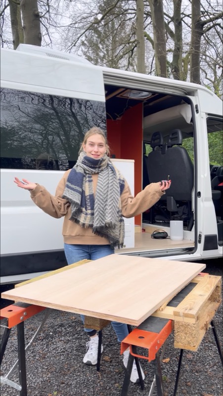 Saskia in front of the open sliding door of the van, arms wide, with a worktop on trestles